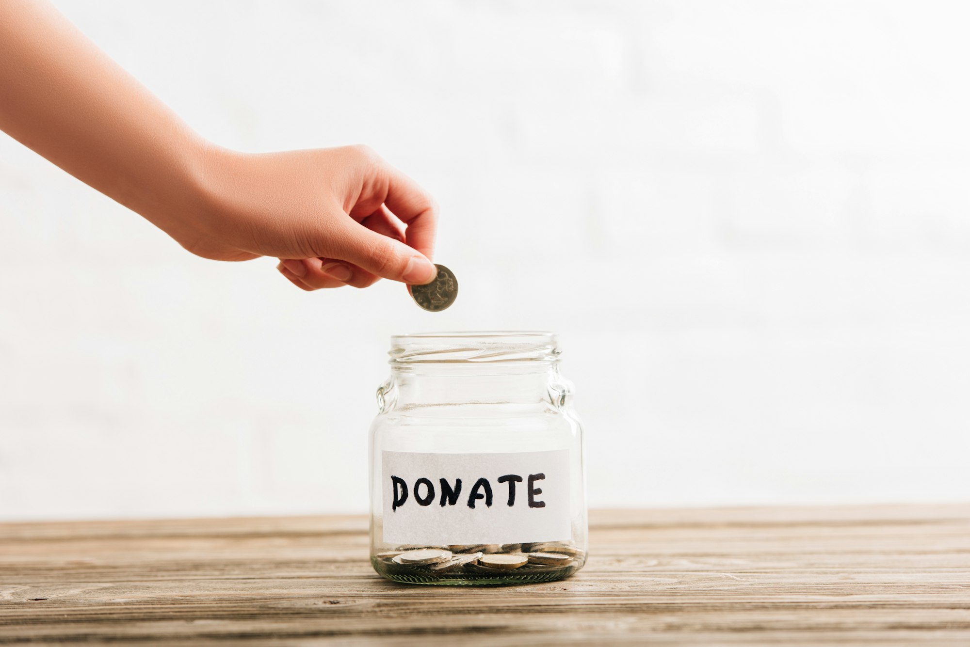 cropped view of woman putting coin in penny jar with donate lettering on wooden surface on white